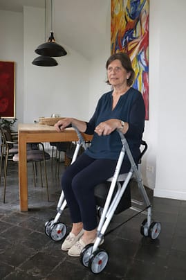 An elderly woman is seated safely on a rollator