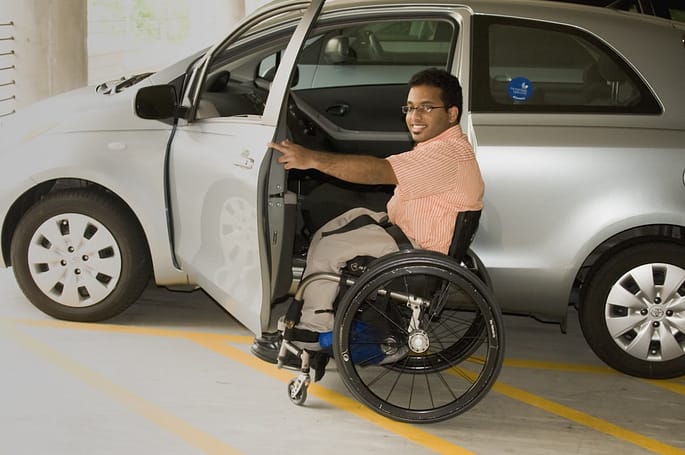 Photo by CDC a man in a wheel chair next to a car; how to put a wheelchair in a car